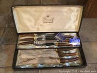 Open box view showing five steak knives and two larger cutting tools with faux bone handles inside satin-lined interior with Crown Chest Sheffield logo.
