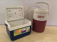 Photo showing small blue and white Coleman cooler with lid removed alongside red and white Coleman thermos with handle