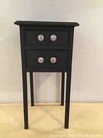 Full front view of small black wooden table with 2 drawers against a white wall