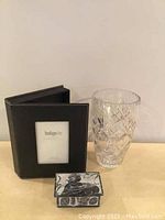 Photo shows a cut crystal vase, black leather photo album, and a rectangular stone box with deer carved on top.