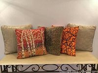 Five decorative pillows displayed side by side, showing variety in color and pattern, including beige and orange tones.