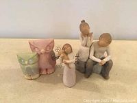 Image showing two Willow Tree figurines of a boy and girl sitting, one Willow Tree angel figurine with wings holding a harp, and two ceramic owl figurines in green and pink colors.