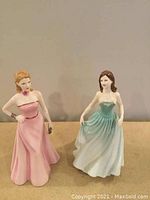 Photo of two Royal Doulton porcelain figurines, Olivia in pink dress and Faye in green dress, side by side on a plain surface.