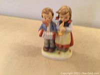 Front view of porcelain figurine showing boy and girl standing together.