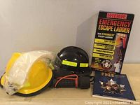 View of all items in the lot including the Kidde Emergency Escape Ladder in packaging, two safety helmets, a flashlight, and a TPS annual book.