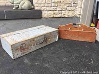 Photo of two wooden carpenter boxes positioned outdoors on pavement in front of a stone wall, showing exterior condition and style.