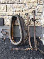 Photo showing antique leather horse neck collar alongside metal harness hames and hooks against a stone wall.