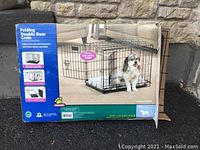 Photo of the dog crate in its original box, showing product photo of wire crate in use with a dog inside. Box states it is a folding double door crate designed for dogs 12-25 lbs.