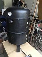 Front angle of the smoker showing the domed lid with thermometer, vent controls, and overall structure.