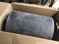 Black polymer lawn roller drum inside a cardboard box, showing some surface wear.