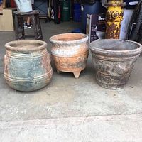 Front view showing three large clay planters with various finishes and decorative embossed details.