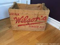 Side view of wooden crate showing 'Drink Wilson's Since 1915 Ginger Ale' in red paint.
