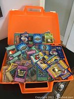 Open orange carrying case filled with assorted Pokémon and Digimon cards loosely arranged inside.