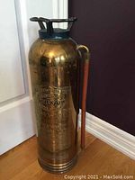 Front and side view of vintage brass fire extinguisher showing engraved General Fire Guard branding and copper hose.