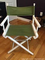 Front angled view of 1970s wooden folding director's chair with white frame and green fabric seating, showcasing condition and style.