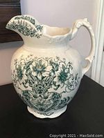 Full view of the antique ceramic water pitcher showing green floral decoration and ornate handle.