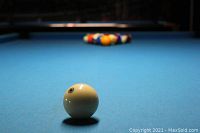 Close-up photo of a pool table with a white cue ball in the foreground and racked colorful pool balls in the background.