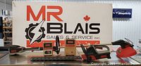 All components of Oregon battery-powered multi-tool kit arranged in front of MR Blais sign