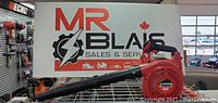 Red and black leaf blower in front of MR Blais Sales & Service sign