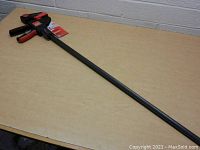 Full view of the Bessey 36 inch trigger clamp laid on a table, showing the long black bar and clamp jaw with trigger handle.