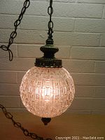 Front view of the illuminated textured glass globe hanging lamp, showing the warm light and metal ornate fittings.