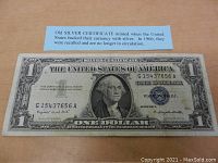 Close-up of 1957 United States one dollar silver certificate bill in good condition with blue seal and serial number G15437656A, along with an informational card about silver certificates.