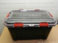 Front angled view of Husky 20 gallon storage container showing clear lid with red latches and black base.