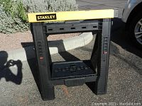 Front view of folding Stanley saw horse, showing yellow top bar and black plastic legs with red adjustment sliders.