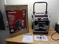 Husky 4.5 Gallon Silent Air Compressor in black and silver, with original box and instruction manuals displayed on table.