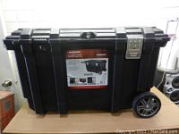Front view of the Husky job box showing lock, keyhole, wheels, and the missing metal latch on the right front corner.