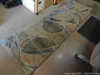 Full view of runner rug on carpeted floor, showing abstract circular and curved pattern in muted colors.
