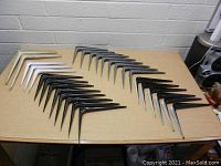 Shelf brackets arranged neatly on a table, showing white, black, and metallic silver brackets in varying sizes.