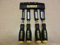 Photo showing front view of four DeWalt chisels in a black plastic holder, handles black and yellow with DeWalt logo, blades of varying widths.