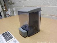 View of translucent gray plastic liquid foaming soap dispenser with gray push lever on table.