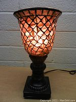 Front view of the lamp lit up, showing the mosaic glass shade and the detailed carving on the dark base.