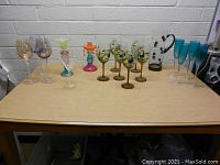 Front view of all glass pieces including colorful wine glasses, teal champagne flutes, and the clear pitcher with black swirl handle.