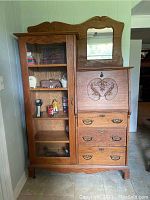 Full view of the carved wood wardrobe with glass cabinet door, mirror, drawers, and pull-down desk closed.