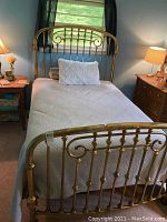 Full view of the brass bed frame assembled with mattress, showing headboard and footboard in a bedroom setting.