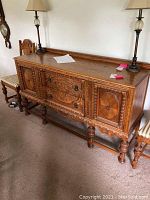 Front view of wooden buffet showing detailed carved doors and drawers with metal handles and keyhole escutcheons.