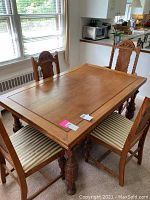 Rectangular wooden dining table with carved legs and slide leaves in a dining room near window.
