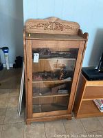 Front view of wooden display cabinet with glass door revealing three shelves and some displayed items inside.