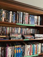 Wide view of DVD collection on wooden shelves showing rows and stacks of assorted movie DVDs.