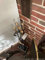 Full view of fireplace tool set with brass-capped handles and black metal stand in front of brick fireplace.