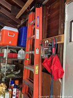 Side view of the orange Werner utility ladder standing upright in a garage, showing height and surrounding objects for scale.