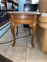Side view photo of oval wood side table showing the cabriole legs and drawer on the apron.