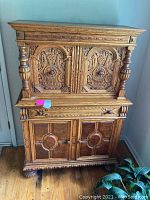Front view showing ornate carved details on upper and lower cabinet doors, drawer, and decorative rounded feet.