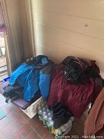 Blue and red ski jackets with gloves and water bottles beneath them on the floor