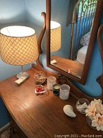 Wide shot of table lamp on wooden table with mirror and assorted small decor including glass bowls, candles, and ceramic spoon rest