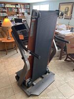 Folded treadmill viewed from side, showing wood-tone running deck base with black track and silver frame