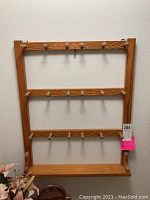Front view of wooden wall shelf with three rows of wooden hooks, mounted on a wall.